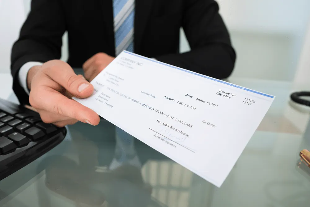 A man in a suit holding out a check.