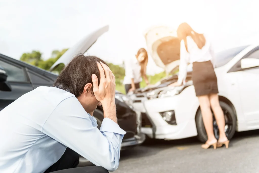 Man holds head in distress next to car crash aftermath. Our team of auto accident lawyers in Kansas City can help you if you’ve recently been injured in an auto accident. 