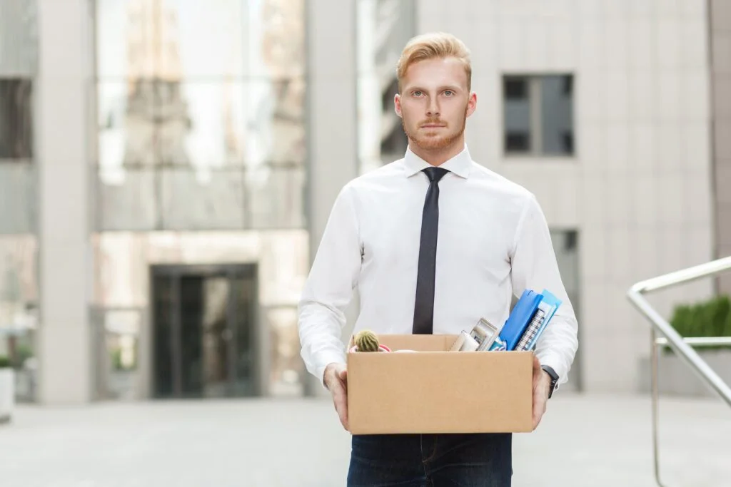 A man holding a box of his belongings from work because he was fired without any warning from his job and needs to hire a wrongful termination lawyer in Kansas City.