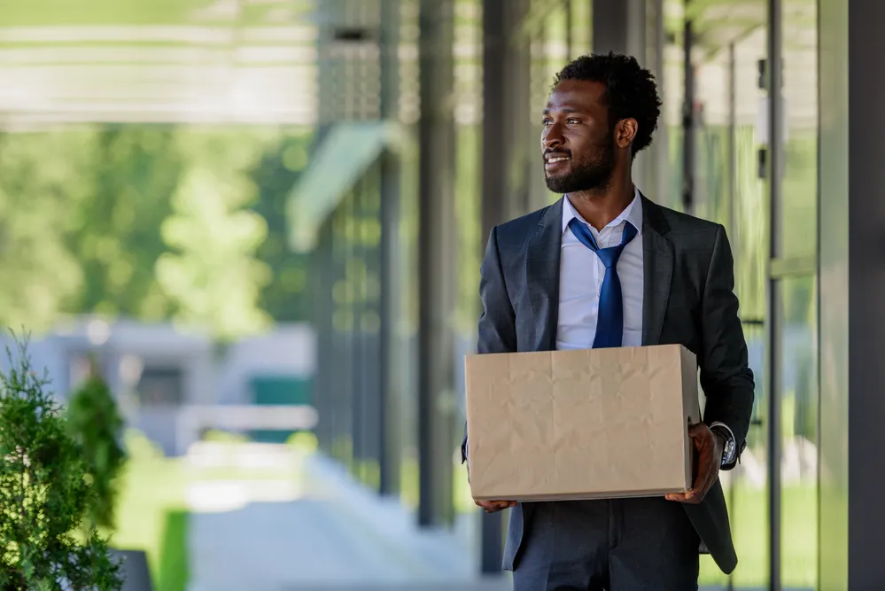 A man in a suit with his tie loosened carrying a box.