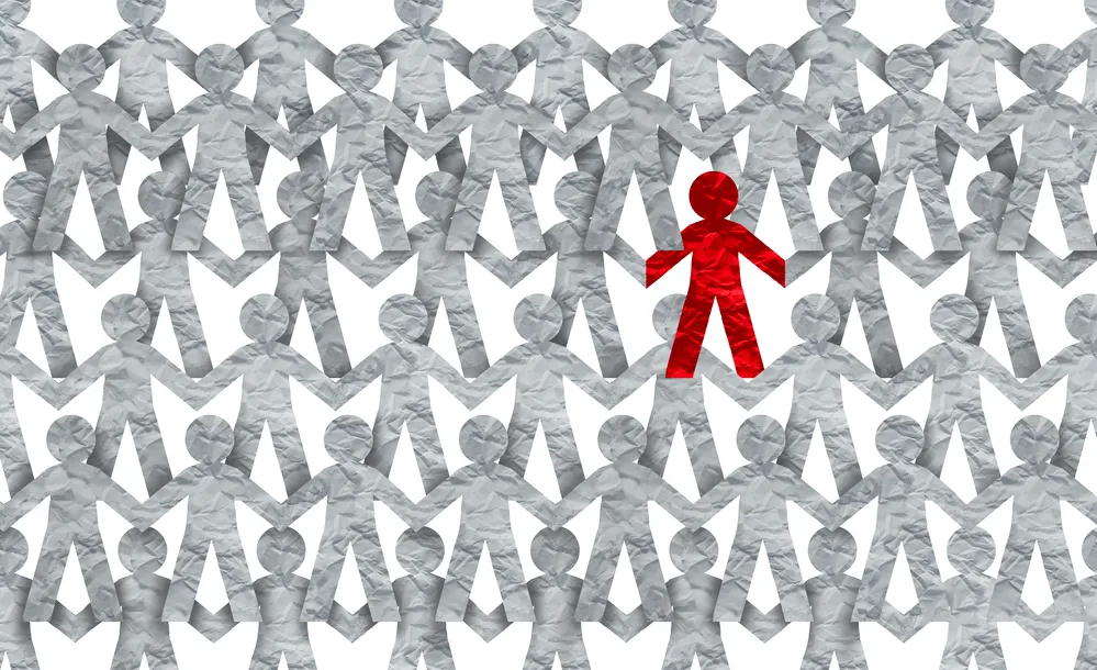 Rows of cutout white paper, cut as people holding hands with a red colored person in the center.