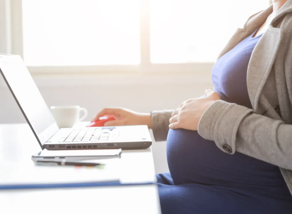 A pregnant woman typing on her computer.