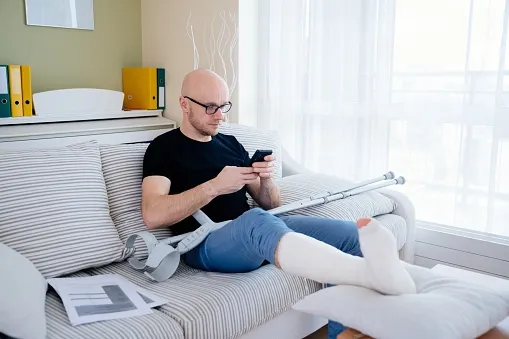 An injured man with a leg cast and is on his phone.