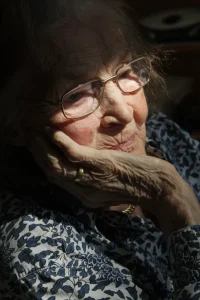 A sad elderly woman looking out of a window.